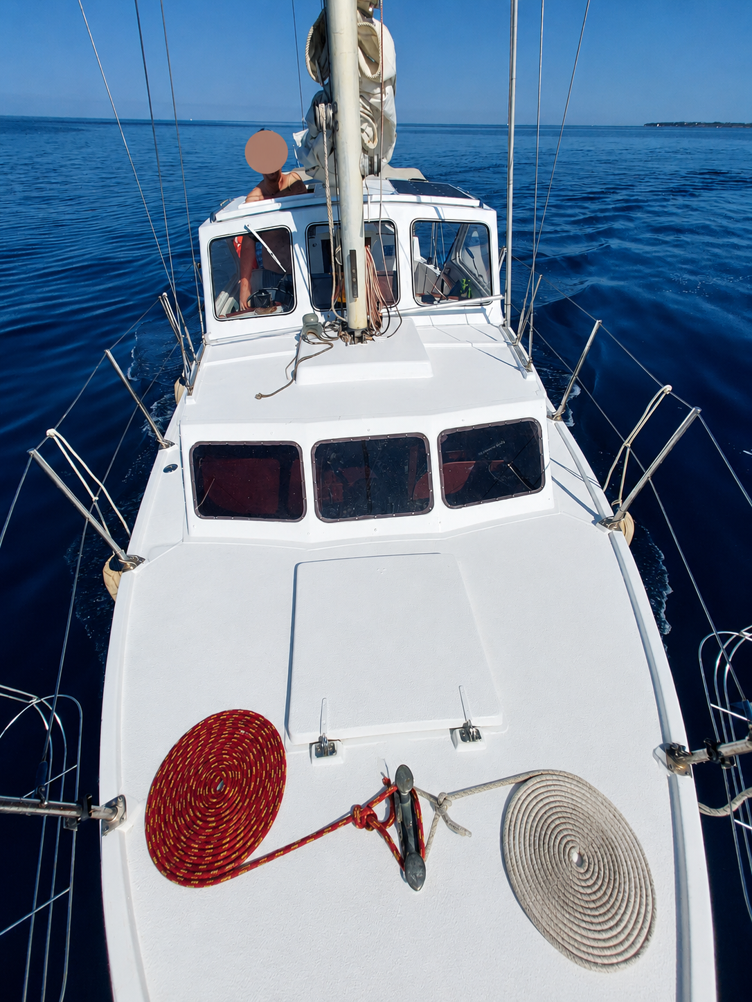 View from STRIGA's bow while under sail, ropes coiled on deck, coastline on the horizon